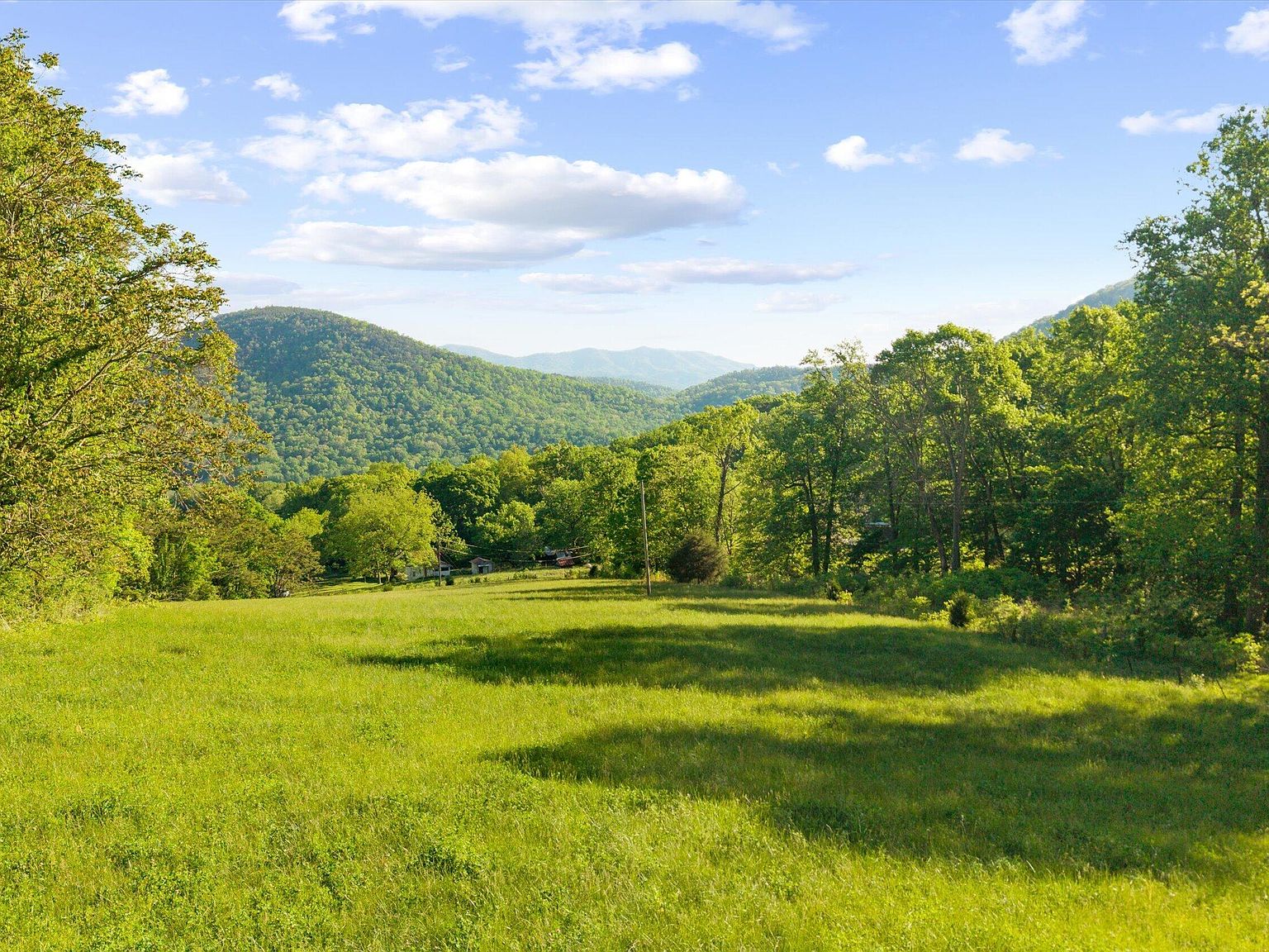 A grassy building site at 172 Pam Lane opening through a gap in the tree line to distant blue mountain ridges