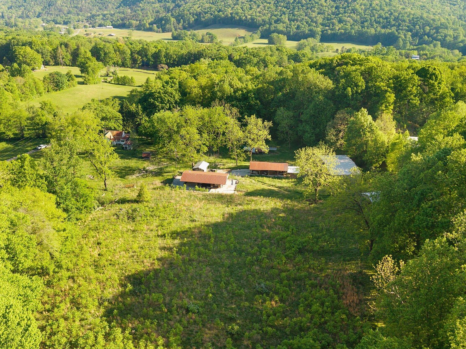Aerial of the existing outbuildings on the property, a red-roofed structure and smaller buildings set in a cleared area with the valley and ridges behind